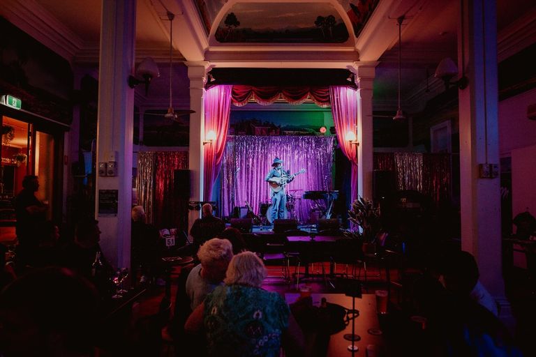 Musician Baeden Faint playing guitar on stage with pink curtains at The Palace Hotel in Broken Hill.